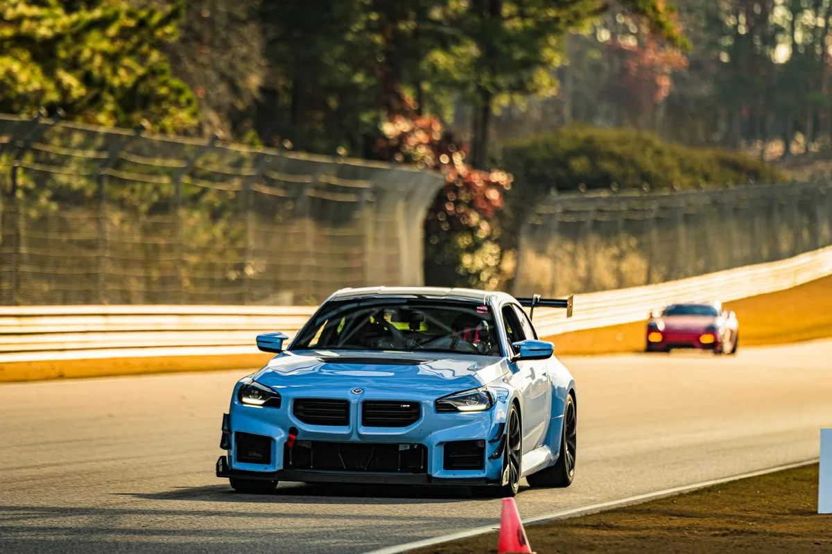 Light blue BMW M2 track car turning in ahead of a chasing car at golden hour